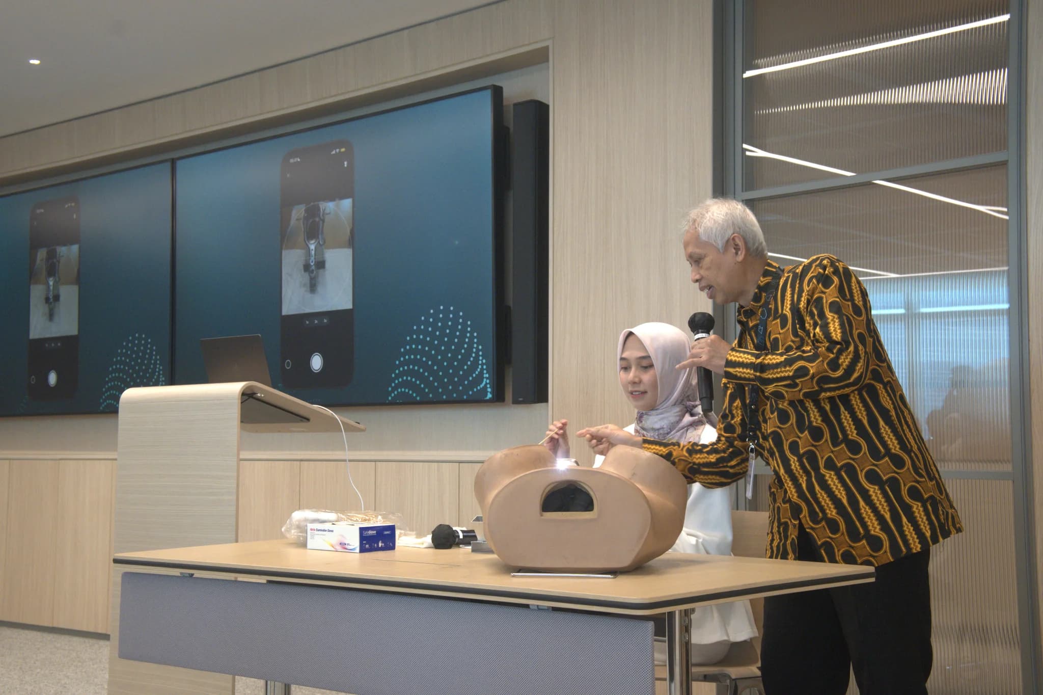 A trainer demonstrating HerLens on a pelvic model while the app is shown on screen