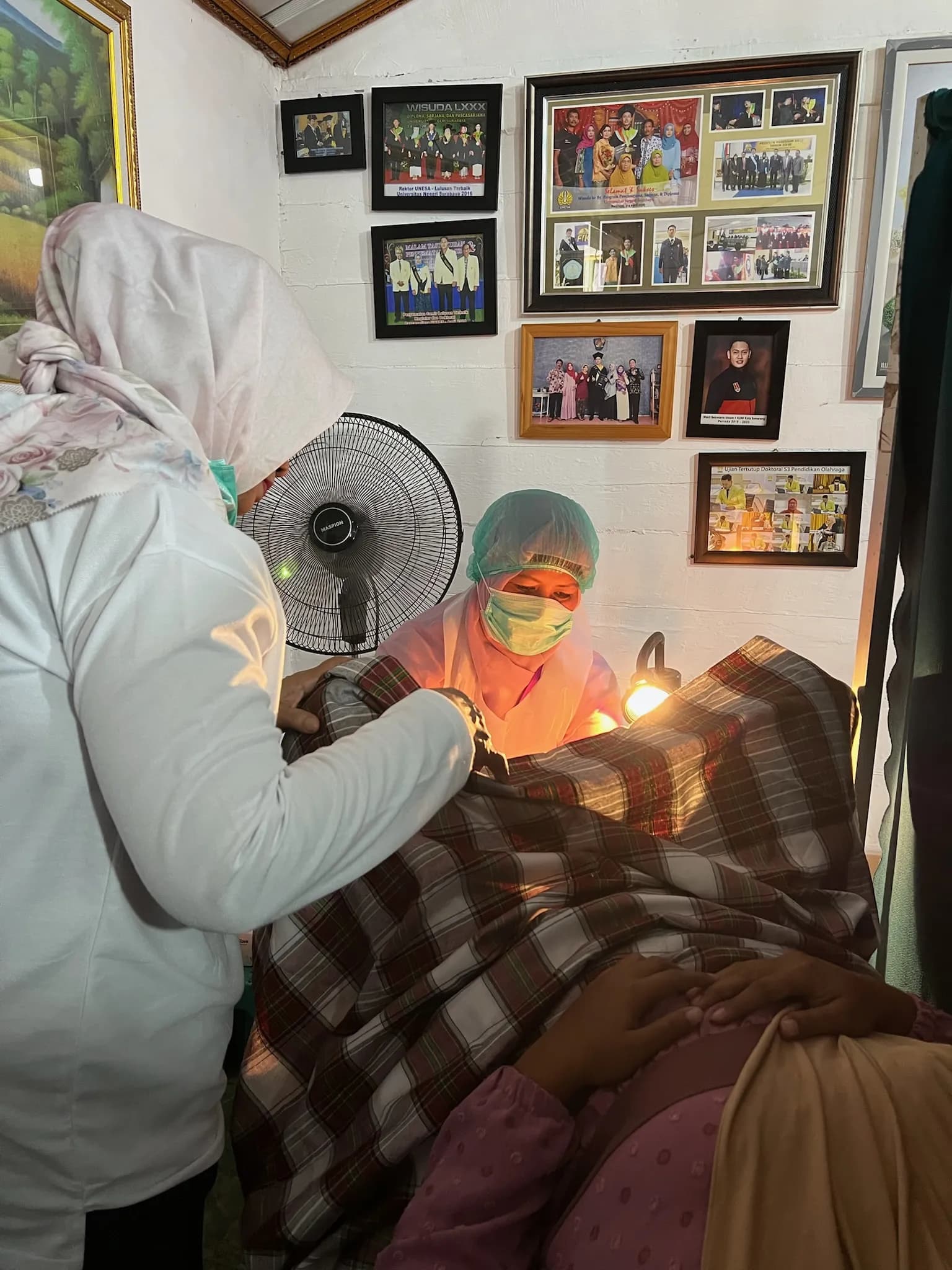Seorang tenaga kesehatan bermasker dan berpenutup rambut melakukan pemeriksaan IVA di bawah cahaya lampu