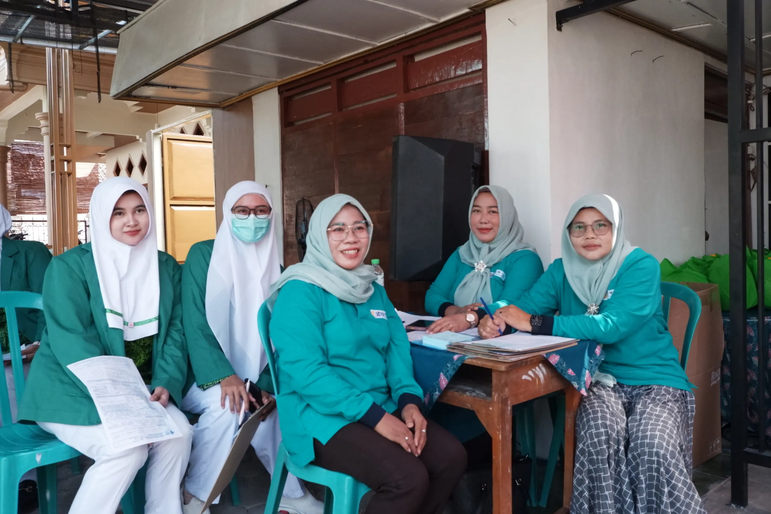 Tenaga kesehatan berseragam hijau toska duduk di meja pendaftaran skrining