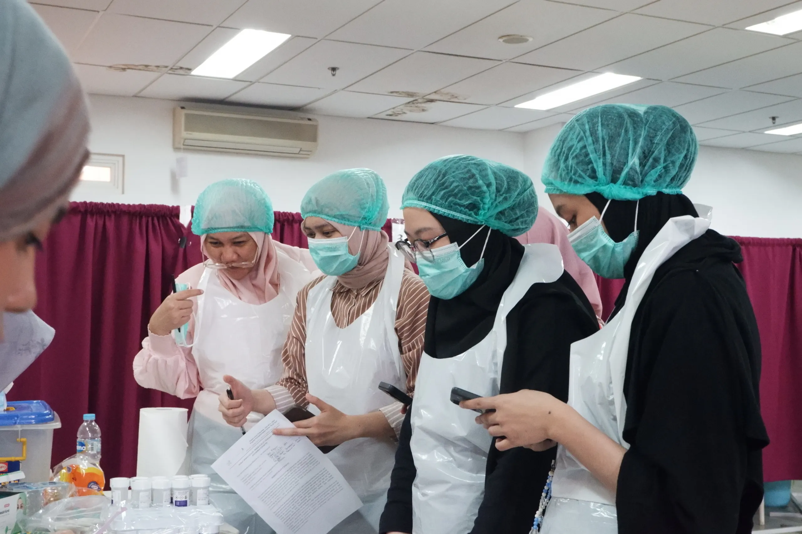 Tenaga kesehatan bermasker dan bercelemek menggunakan ponsel pintar saat pelatihan praktik langsung