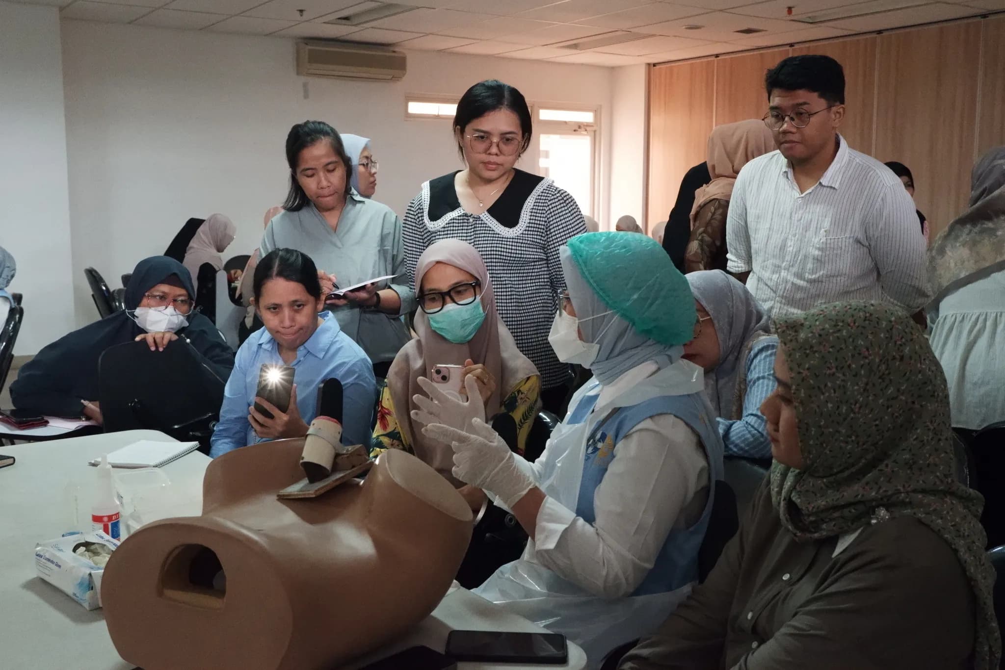 A trainer demonstrating the VIA exam on a pelvic model to health workers holding their smartphones