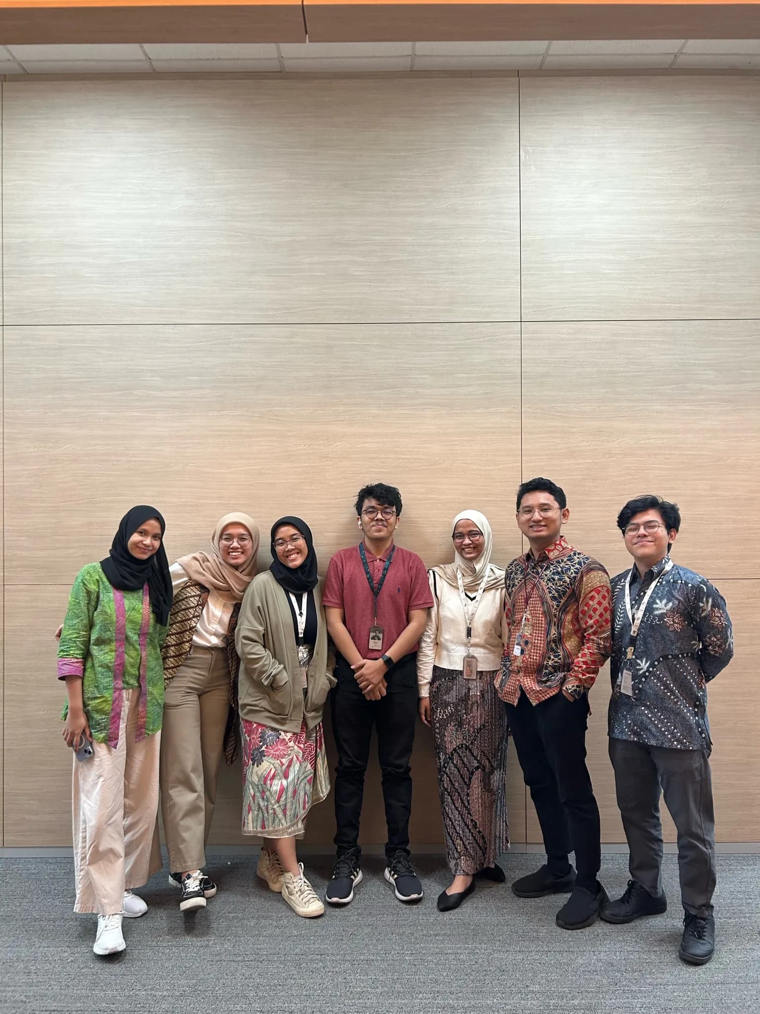 Tim HerLens berdiri bersama di depan dinding berpanel kayu