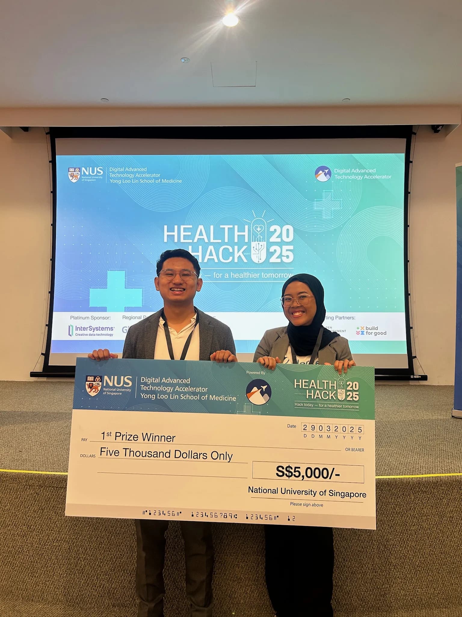 Dua pendiri HerLens memegang cek juara pertama di NUS HealthHack 2025