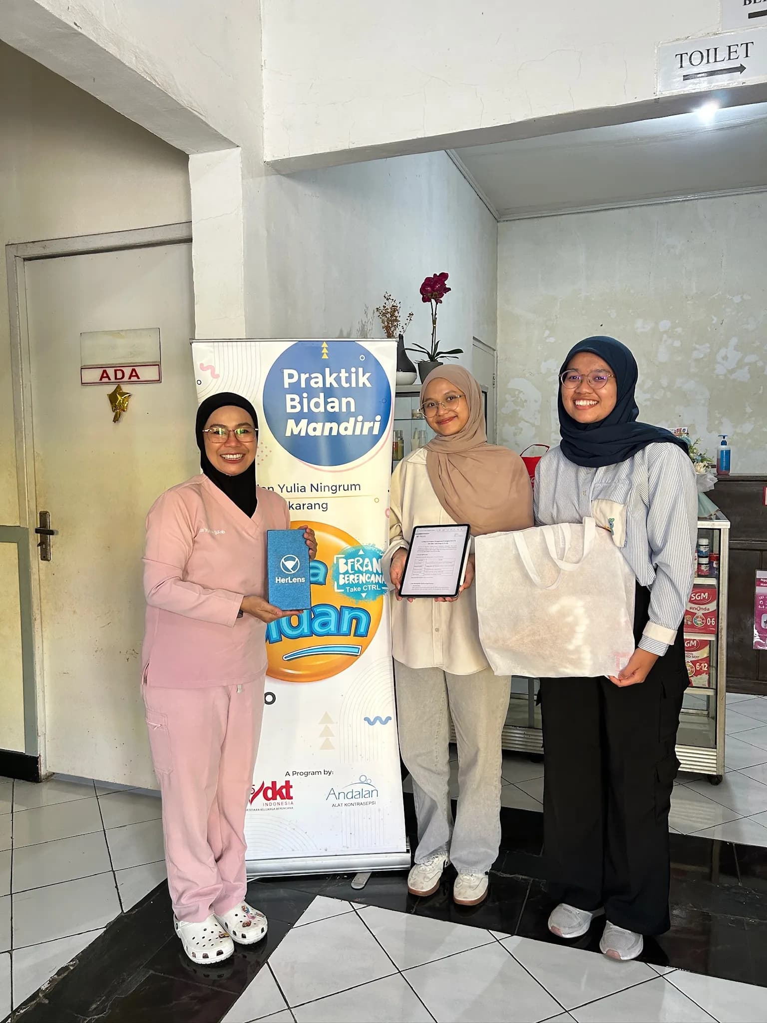 Seorang bidan memegang kit HerLens bersama tim HerLens di tempat praktik mandirinya